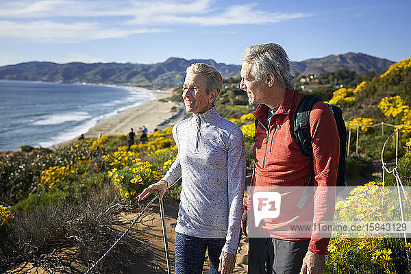 Lächelndes älteres Paar redet im Sommer beim Spaziergang auf einem Berg am Strand gegen den Himmel