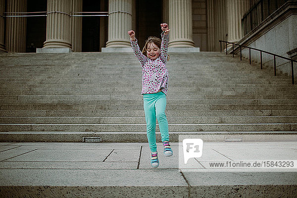 junges Mädchen springt auf einer Treppe vor einem großen Säulengebäude