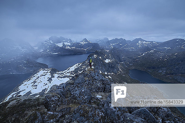 Female hiker takes in view of mountain landscape from summit of Narvtind mountain peak  MoskenesÃ¸y  Lofoten Islands  Norway