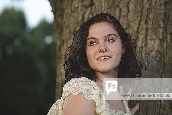 Portrait of a smiling young woman standing against a tree at sunset