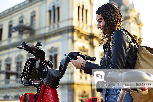 Frau nimmt mit ihrem Handy ein gemietetes Elektrofahrrad mit.