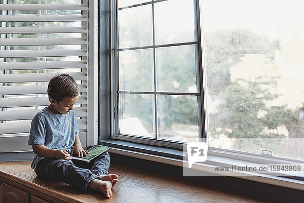 Junge liest in Fensternische mit weichem Licht und Fensterläden