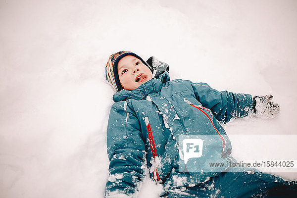 Glücklicher Junge streckt die Zunge heraus  während er im Winter im Schnee liegt