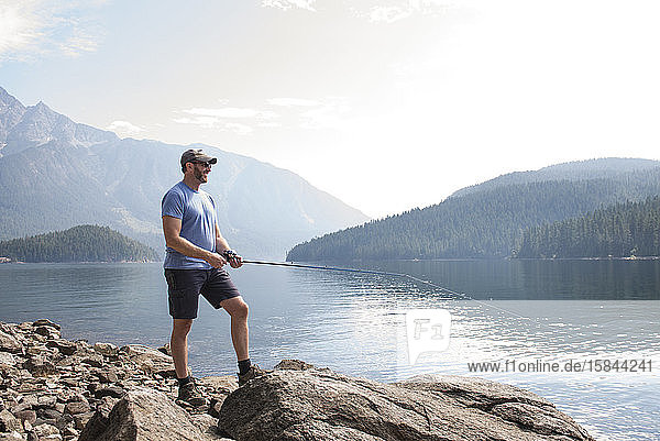 Auf Felsen stehender Mann lächelt und fischt an einem See in Washington