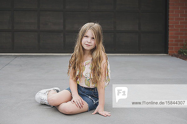 Portrait of a cute young girl sitting in front of a garage door