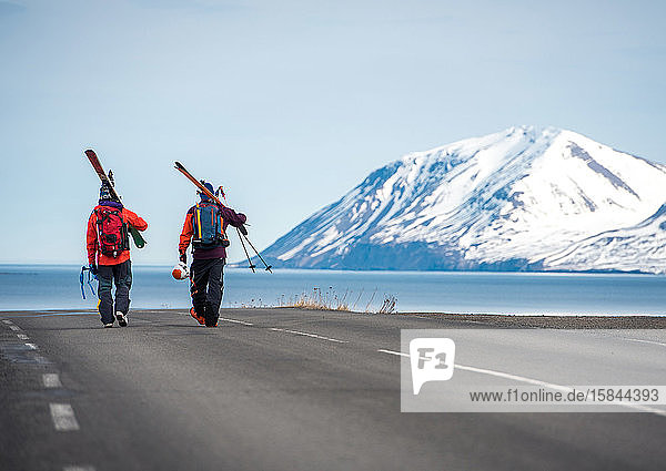 Zwei Männer gehen auf einer gepflasterten Straße in Island mit Bergen und Wasser