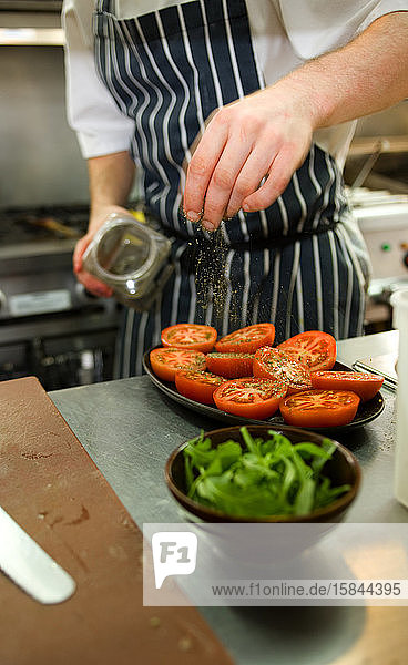 chef sprinkles herbs on tomatoes in restaurant kitchen
