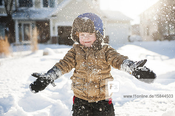 Kleinkind spielt und lächelt beim Schneewerfen vor dem Haus