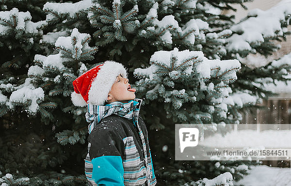 Ein Junge in Santa hat an einem verschneiten Tag Schneeflocken auf der Zunge gefangen.