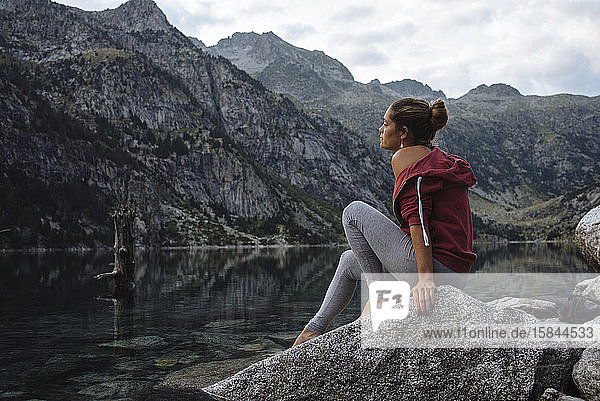 Frau mit Brötchen  die während einer Reise auf einem Felsen an einem See sitzt.