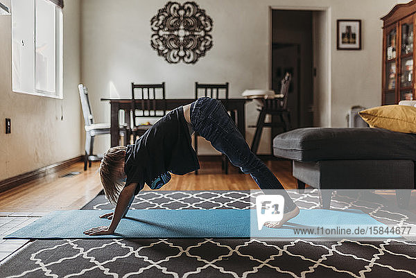 Schulpflichtiger Junge macht während der Isolation Yoga im Wohnzimmer