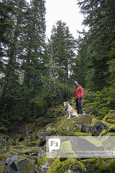 Male hiker and fluffy dog standing on mossy rocks in the mountains