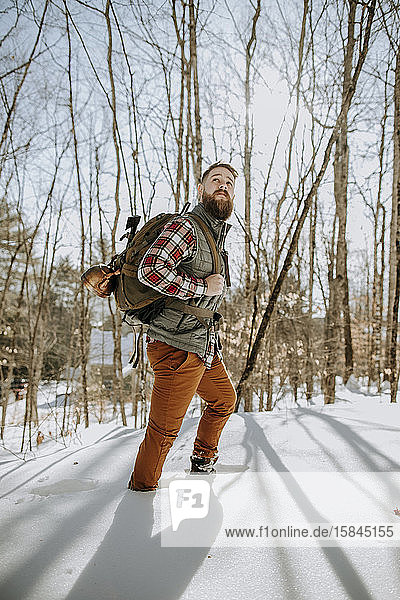 man with beard wearing flannel hikes through snow in Maine woods