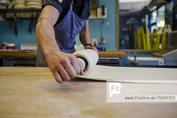Ein Bäcker rollt den Teig auf eine bemehlte Holzplatte