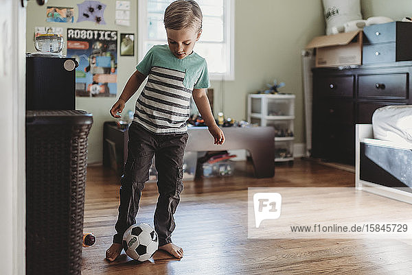Barefoot boy wearing striped shirt with soccer ball on wood floor