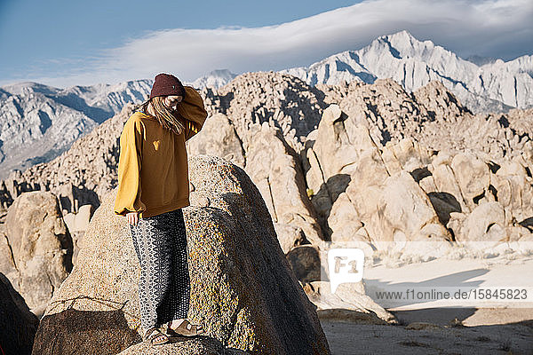 Frau steht auf Felsen im Wind in der Nähe von Bergen