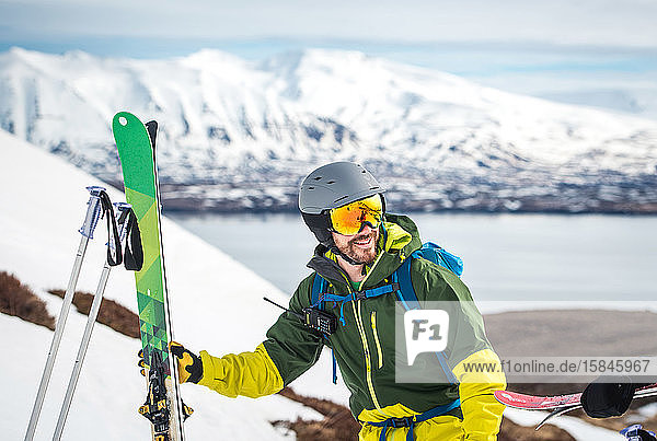 Ein Mann mit Skiausrüstung und Bergen und Wasser im Rücken