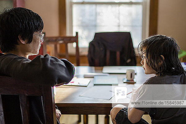 A boy and father sit at a dining room table talking together