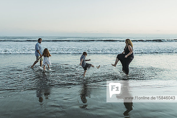 Vierköpfige Familie  die in der Abenddämmerung im Meer spielen und sich gegenseitig bespritzen