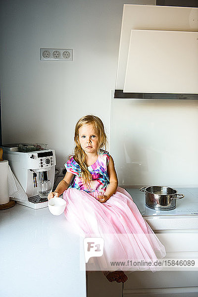 Kleines Mädchen in einem schönen Kleid  das auf dem Küchentisch sitzt