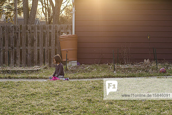 Ein fokussiertes kleines Mädchen sitzt bei Sonnenuntergang auf einem Pfad im Hof und schreibt einen Brief