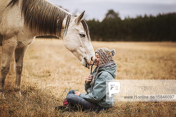 Happy horse licking young girls face in a field in the fall
