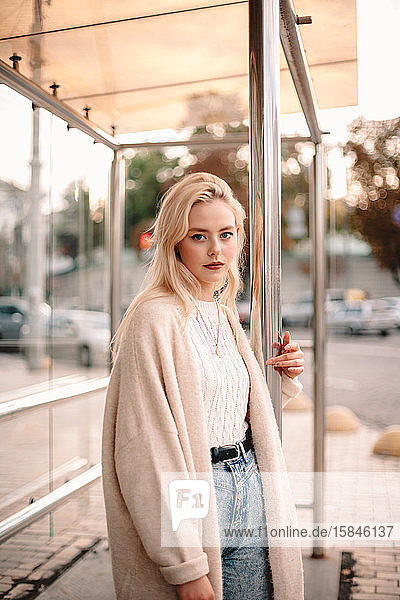 Bildnis einer jungen Frau mit blonden Haaren an einer Bushaltestelle in der Stadt stehend