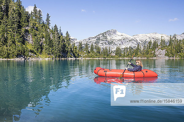 Pensionierte Frau paddelt während einer Reise mit einem roten Boot auf einem abgelegenen See.