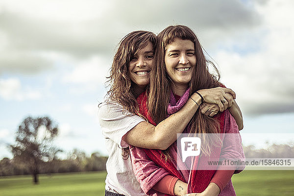 zwei Freundinnen umarmen und lachen im Freien auf grünem Farmland