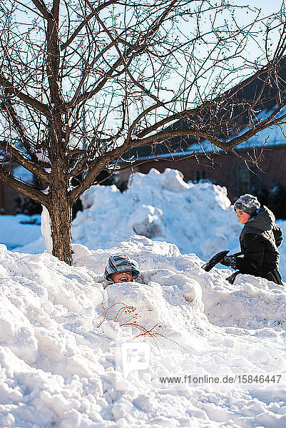 Zwei Jungen bauen an einem sonnigen Wintertag mit Schaufeln Schneefestungen.
