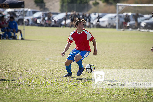 jugendlicher Fußballspieler in rot-blauer Uniform  der den Ball während eines Spiels kontrolliert