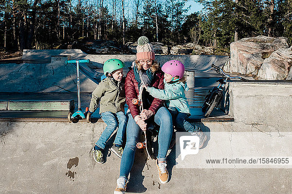 mom playing with her kids at a skatepark riding bikes and scooters