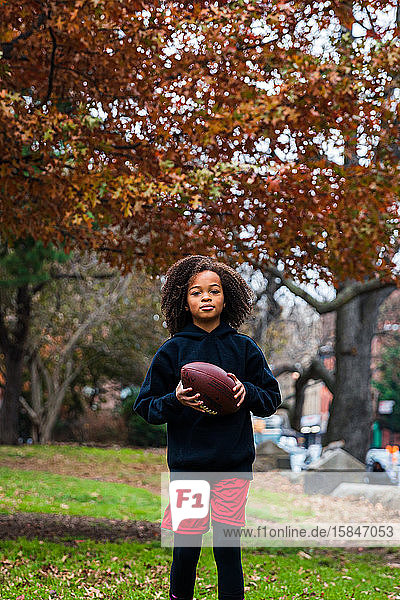 Portrait of confident girl practicing American football at park in city