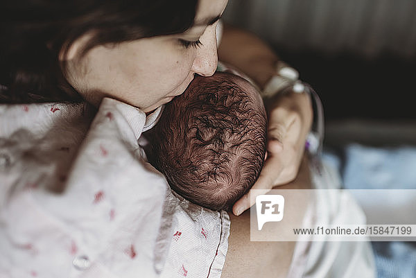 Mitteansicht der Mutter im Krankenhausbett  die den Kopf des neugeborenen Sohnes küsst