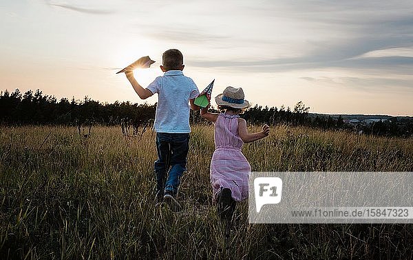 siblings running through a meadow together playing at sunset