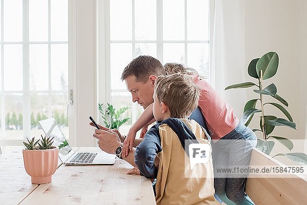 father working from home with his kids climbing over him