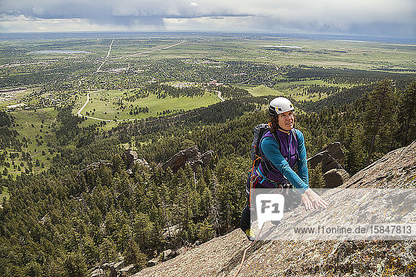 Woman rock climbs Fifth Flatiron as rain falls over Boulder  Colorado