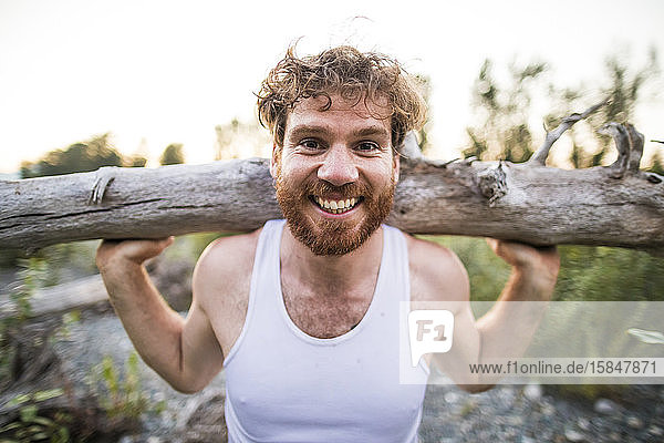 portrait of man balancing log on shoulders during an outdoor workout.
