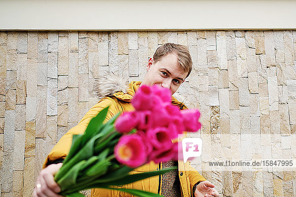 blonder Mann in einer gelben Winterjacke mit einem Tulpenstrauss in der Hand