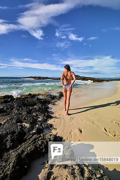 Eine Frau bürstet den Sand von ihrem Bikini  während sie an Makalawena entlang geht