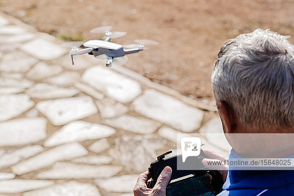 Rückansicht des älteren Mannes  der die Drohne steuert und im Stehen auf das Display der Fernbedienung schaut