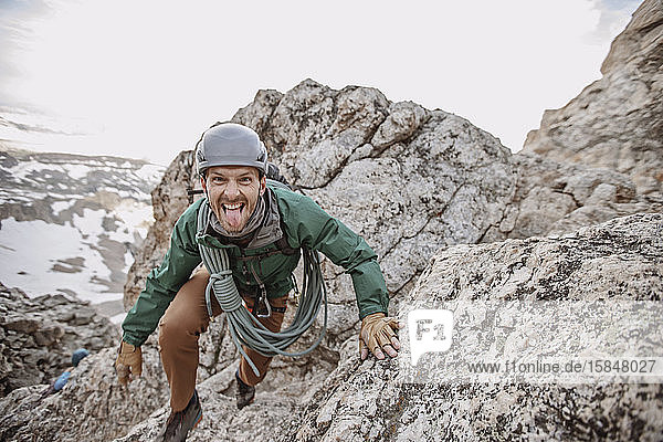 Male rock climber with rope and helmet sticks tongue out