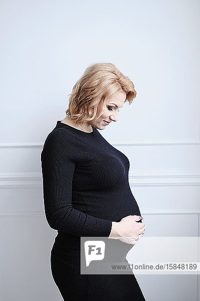 schwangere Frau in schwarzem Kleid  die lächelnd den Bauch berührt