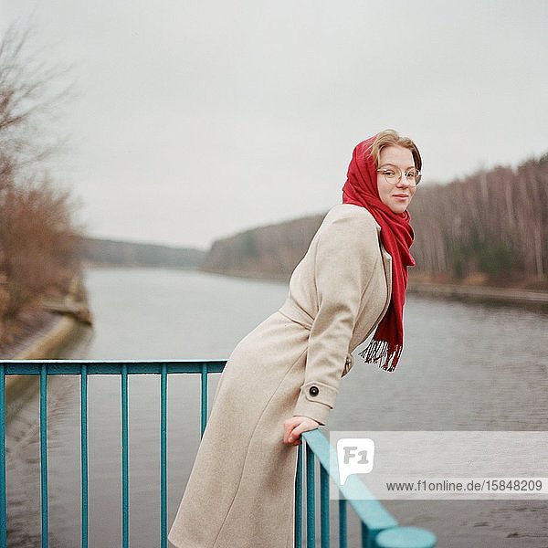 A woman stands on the riverbank in a red scarf