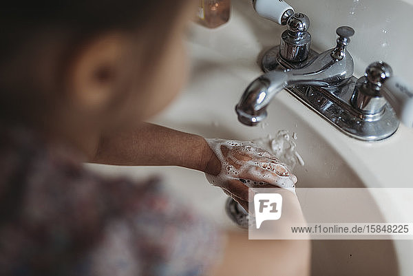 Hoher Winkel eines Mädchens im Vorschulalter beim Händewaschen im Waschbecken mit Seife