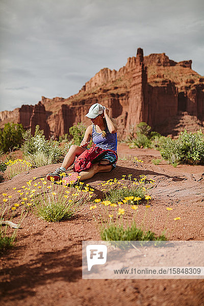 Wanderfrau richtet ihren Hut  während sie zwischen gelben Wüstenblumen ruht