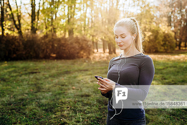 Fitness im Park: Das Mädchen hält Smartphone und Kopfhörer in der Hand.