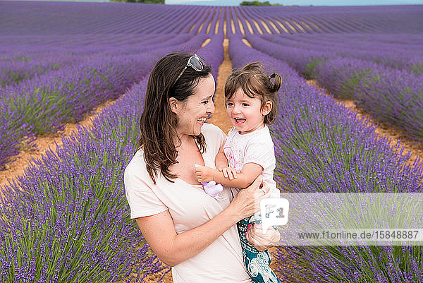 Glückliche Mutter und Tochter spazieren im Sommer zwischen Lavendelfeldern