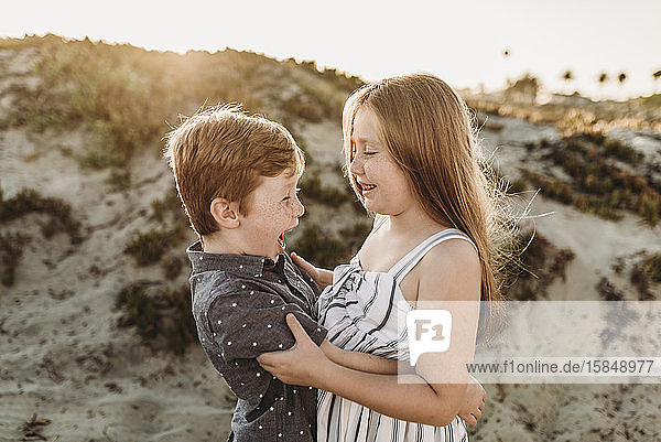 Side view of young brother and sister hugging and laughing at beach