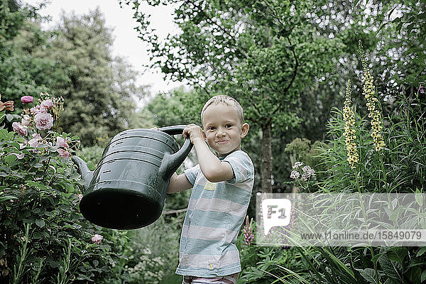 Porträt eines jungen blonden Jungen  der seinen englischen Bauerngarten bewässert